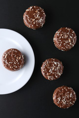 Chocolate cookies with coconut shaving chocolate coating and coconut on wooden black  background.