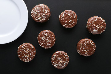 Chocolate cookies with coconut shaving chocolate coating and coconut on wooden black  background.