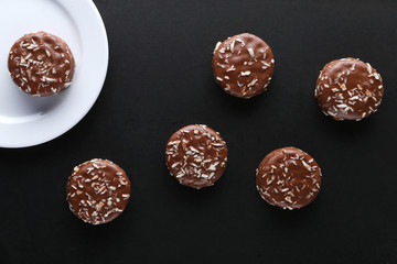 Chocolate cookies with coconut shaving chocolate coating and coconut on wooden black  background.