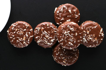 Chocolate cookies with coconut shaving chocolate coating and coconut on wooden black  background.