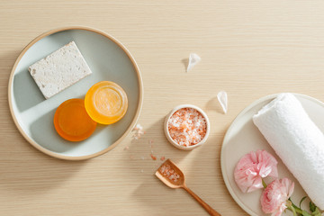 Top view of organic spa skincare products with salt, flowers, natural soap, towels and pumice stone