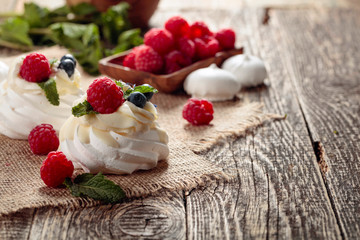 Dessert Pavlova with raspberries, blueberries and mint on a old wooden table.