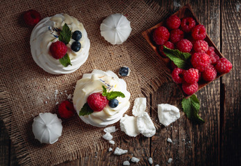 Dessert Pavlova with raspberries, blueberries and mint on a old wooden table.