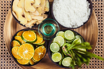 Natural organic ingredients for spa, bath and scrub: slices of fresh ginger, orange, lime, sea salt and oil for beauty treatment. Wooden background, top view.