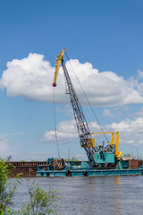 Fototapeta premium vertical banner of barge with a crane on the river with green trees and blue sky on the background