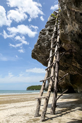 Wooden ladder to climb up to the rock on the beach with seaside and blue cloudy sky in the background, stairway to heaven