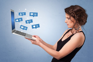 Woman holding laptop with different types of social media symbols and icons