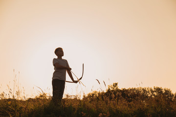 Black silhouette of young caucasian kid isolated on sunny golden sunset sky background. Boy playing...