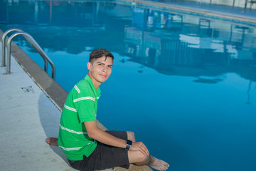 Young guy poses sitting at the border of a swimming pool.