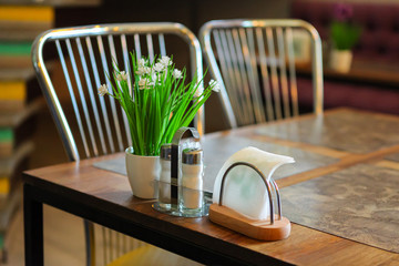 Empty table with a set of napkins and spices: salt and pepper next to a bouquet of flowers....