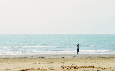 Fototapeta na wymiar Single Asian girl walking along sea coast