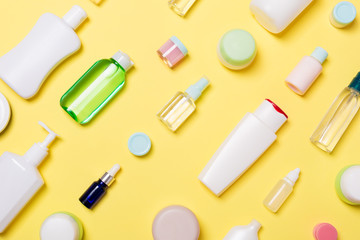 Top view of different cosmetic bottles and container for cosmetics on yellow background. Flat lay composition with copy space