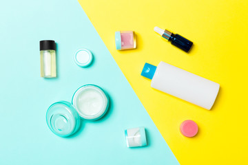 Top view of cosmetic containers, sprays, jars and bottles on yellow and blue background. Close-up view with empty space for your design