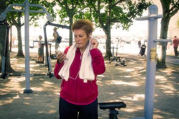 senior woman resting with mobile phone after exercising and gymnastics