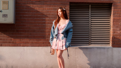 Street photography of a cute Chinese young woman in jeans and pink dress with red brick wall background in sunny day, female portrait, sexy girl.