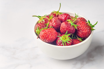 Fresh organic strawberry in the white bowl and fork, on the white background.