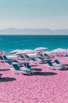 Beach with pink sand, blue sunbeds, sea and mountains. Infrared style. Creative concept