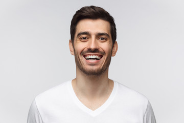 Handsome cheerful smiling broadly unshaven young man in white t-shirt laughing out loud