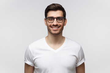 Eyewear fashion. Portrait of smiling handsome young man in casual white t-shirt and trendy glasses, looking at camera, isolated on gray background