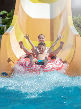 European lady and her son are enjoying their vacations. They are having fun in waterpark. They sliding down slide in aqua park.