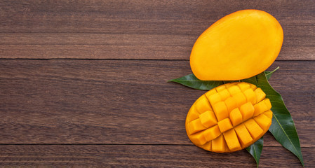 Fresh mango - beautiful chopped fruit with green leaves on dark wooden timber background. Tropical fruit design concept. Flat lay. Top view. Copy space