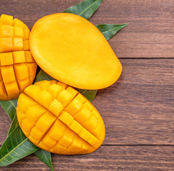 Fototapeta premium Fresh mango - beautiful chopped fruit with green leaves on dark wooden timber background. Tropical fruit design concept. Flat lay. Top view. Copy space