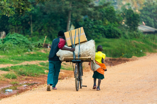 A ugandan man and a child transporting things with a bicycle