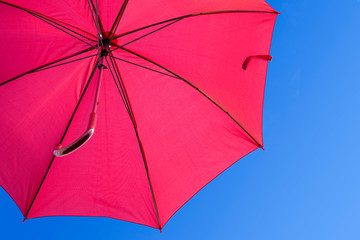 Open red umbrella against a blue sky. Weather forecast.