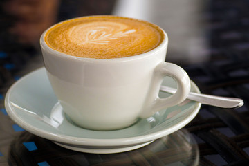 A cup of cappuccino coffee on a glass table in a cafe