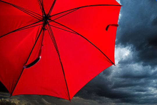 Open red umbrella against the backdrop of a stormy sky. Weather forecast. Red level of danger.
