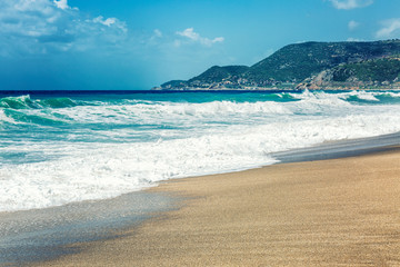 Fototapeta na wymiar Sandy coast of the turquoise sea. Surging waves, sunny windy day. Space for text.