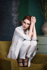 Obraz premium Concept: fashion, beauty. Pretty redhead thin lean young woman with vintage hairdo alluring in white unbuttoned pant suit. Studio photoshoot.