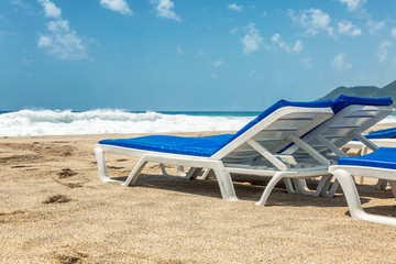 White loungers with blue mattresses on a public sandy beach by the sea. Close-up. Space for text.