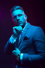 Young handsome model posing in a studio in a trendy neon light. Fashionable man in a stylish suit. Vibrant color. Bright colorful light effects. Disco style. Overlay. Gel filter. Supersaturated