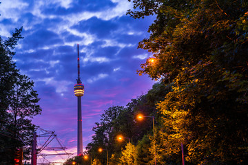 Obraz premium Germany, Night sky over television tower of stuttgart city in green forest nature landscape illuminated by street lights and red sky of afterglow