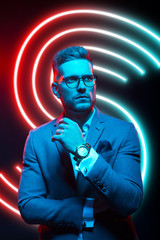 Young handsome model posing in a studio in a trendy neon light. Fashionable man in a stylish suit. Vibrant color. Bright colorful light effects. Disco style. Overlay. Gel filter. Supersaturated