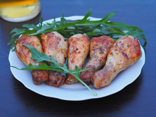 Delicious and beautiful chicken with a golden crust, herb arugula in a white plate and a glass of beer are on a dark background close-up