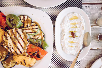 Top down view of Greek food:tzatziki sauce with olive oil and grilled cheese with vegetables in...