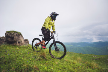 Fototapeta premium Aged male athlete in helmet and mask rides down a grassy slope on a mountain bike. Downhill mountain bike concept