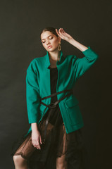 Attractive young girl model with dark hair in a trendy green jacket and jewelry on a black background in the studio