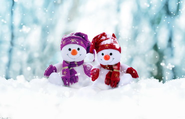 Two little snowmen the girl and the boy in caps and scarfs on snow in the winter. Background with a funny snowman. Christmas card.