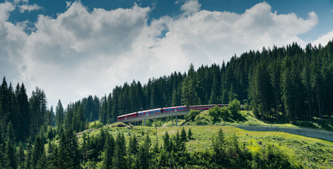 red Rhaetian railway train in a green summer mountain landscape in the Swiss Alps