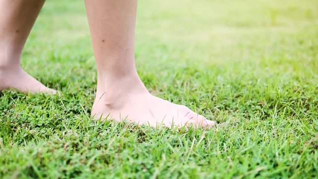 Girl walking with barefoot on green grass with sunlight, slow motion.