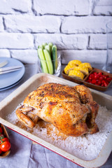 Chicken whole baked on salt. With corn on the cob, cherry tomatoes, cucumbers and jalapeno peppers. Selective focus, close-up.