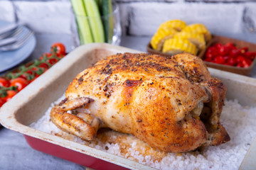 Chicken whole baked on salt. With corn on the cob, cherry tomatoes, cucumbers and jalapeno peppers. Selective focus, close-up.
