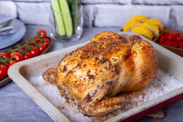 Chicken whole baked on salt. With corn on the cob, cherry tomatoes, cucumbers and jalapeno peppers. Selective focus, close-up.