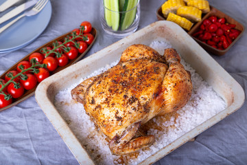 Chicken whole baked on salt. With corn on the cob, cherry tomatoes, cucumbers and jalapeno peppers. Selective focus, close-up.