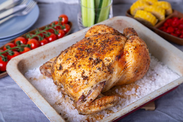 Chicken whole baked on salt. With corn on the cob, cherry tomatoes, cucumbers and jalapeno peppers. Selective focus, close-up.