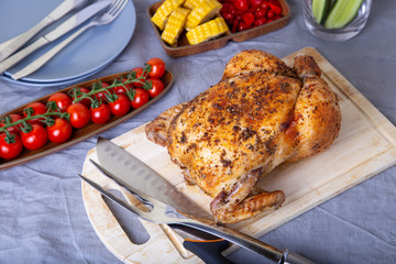 Chicken whole baked on salt. With corn on the cob, cherry tomatoes, cucumbers and jalapeno peppers. Selective focus, close-up.