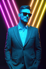 Young handsome model posing in a studio in a trendy neon light. Fashionable man in a stylish suit. Vibrant color. Bright colorful light effects. Disco style. Overlay. Gel filter. Supersaturated